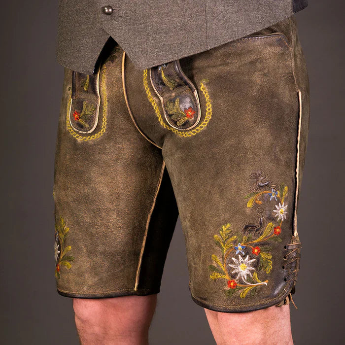 Moderner bayerischer Mann trägt eine kurze Wildbock Lederhose aus hochwertigem Wildleder mit feinen Reliefstickereien, kombiniert mit einem weißen Trachtenhemd – Datschi Trachten Kollektion